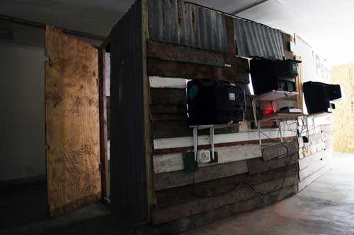 Giorgio Bruni. And What? (rear view), 2010. DVD loop, TVs, projection, wood, corrugated iron, dimensions variable. © the artist.