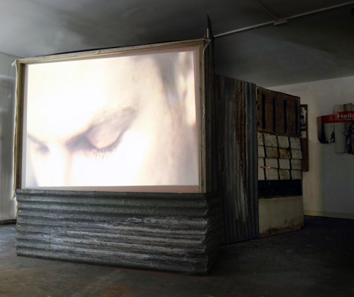 Giorgio Bruni. And What? (outer screen view), </em>2010. DVD loop, TVs, projection, wood, corrugated iron, dimensions variable. © the artist.