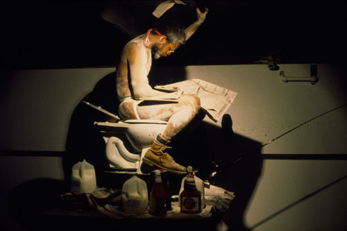 Pope L. performing Eating the Wall Street Journal (2000), The Sculpture Center, New York, 2000. Courtesy the artist. Photograph: Lydia Grey. [Installation on view at Grey Art Gallery, NYU].